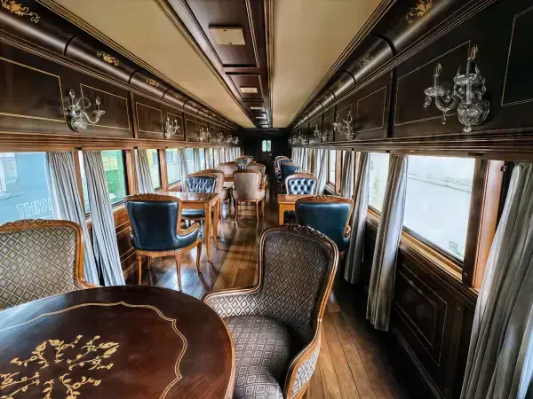Interior do vagão boutique Imperial com mesas para quatro pessoas, abajures e decoração clássica anos 30.