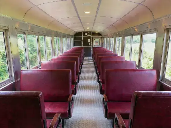 Interior do vagão classe turística com poltronas duplas estofadas e janelas para apreciação da vista.